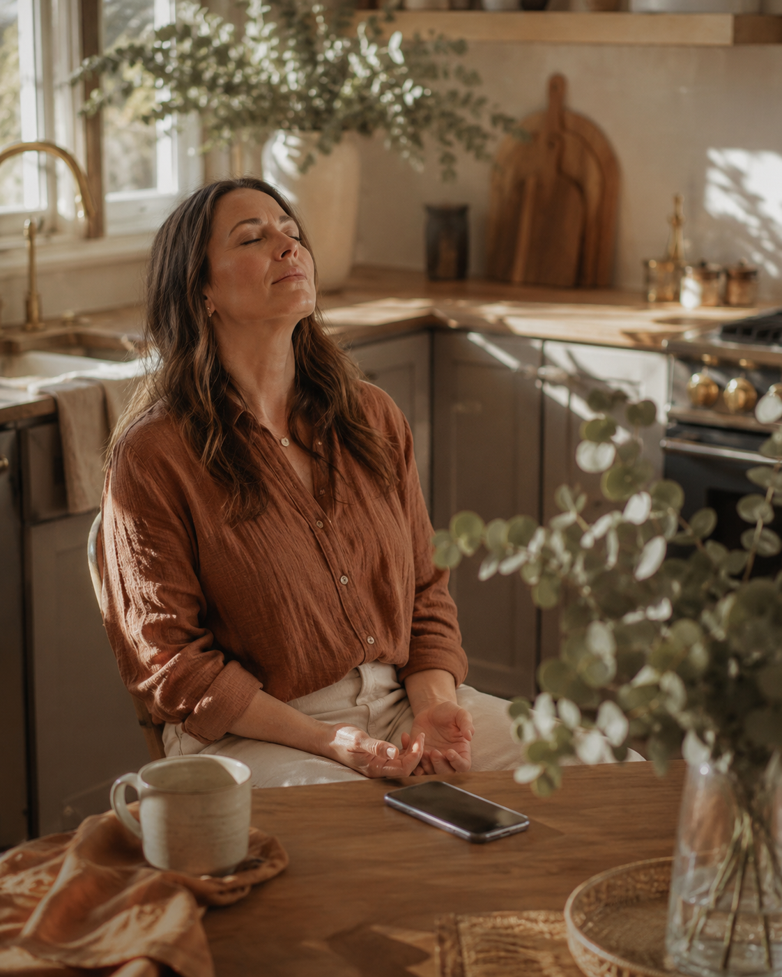 A woman at her kitchen table, eyes closed, phone face-down — the weight finally lifted.